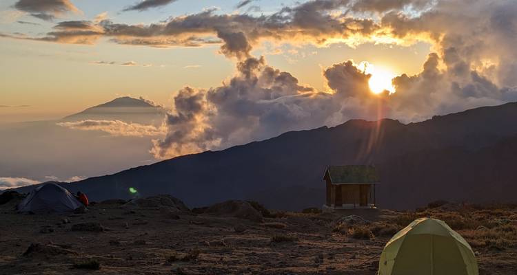 Vista del amanecer sobre las montañas con tiendas de campaña en primer plano.