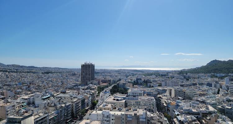 Panoramic view of a city landscape from above, with distant sea.