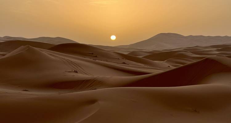 Coucher de soleil sur les dunes de sable avec des traces visibles.