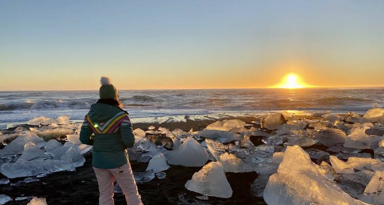 Persoon die op een ijzig strand staat tijdens zonsondergang.