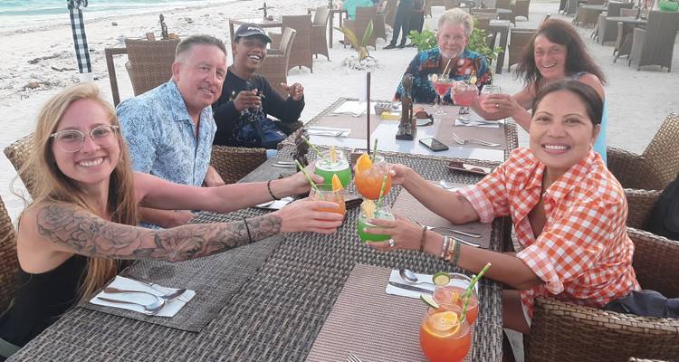 Un groupe de personnes levant leurs verres dans un cadre de repas en plein air près de la plage.