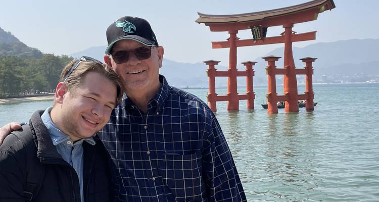 Deux personnes posant avec le Torii flottant du sanctuaire d'Itsukushima en arrière-plan.