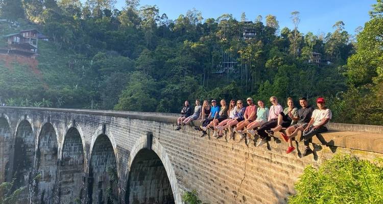 Des gens assis sur un pont historique entouré de verdure.