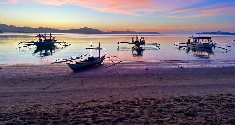Bateaux traditionnels sur une mer calme pendant un coucher de soleil coloré.