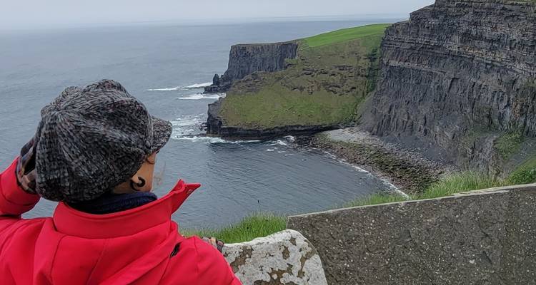 Person with a hat overlooking cliffs and ocean.