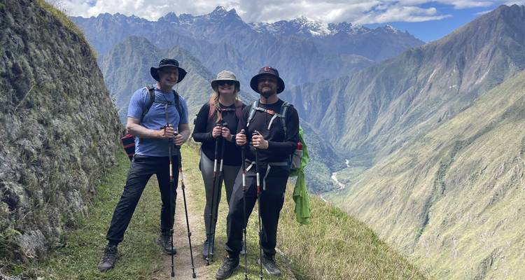 Trois randonneurs avec des bâtons de randonnée sur un sentier de montagne.
