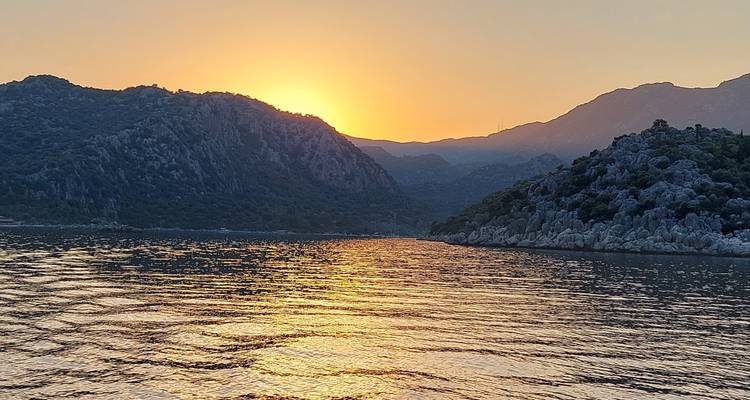 Zon die ondergaat achter de bergen en weerkaatst op het water.