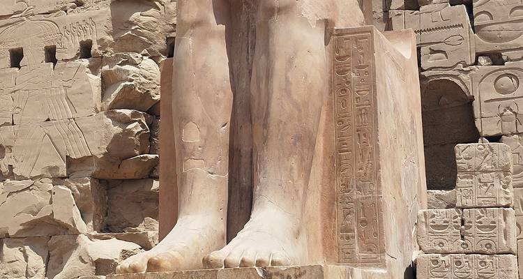 Gros plan des pieds d'une statue égyptienne antique avec des hiéroglyphes.