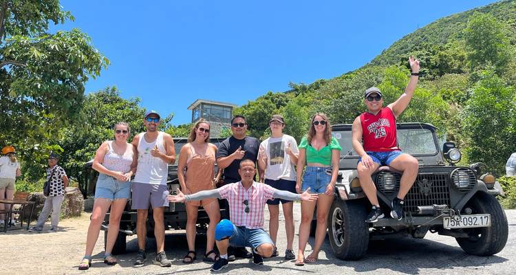 Touristes posant avec une jeep vintage et une montagne pittoresque en arrière-plan.
