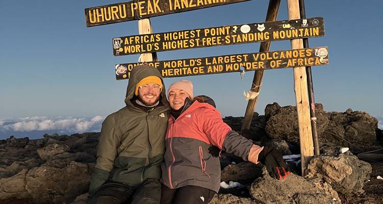 Paar sitzt am Uhuru Peak Schild, Mount Kilimanjaro.