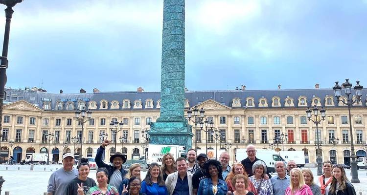 Un groupe de personnes posant à la Colonne Vendôme avec des bâtiments classiques.