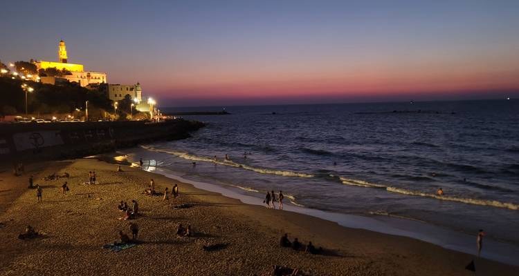 Una playa al atardecer con una torre iluminada en el fondo.