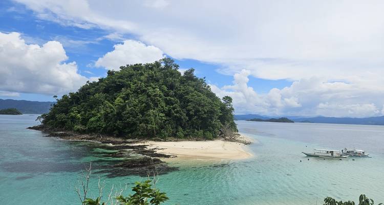 Petite île tropicale avec une plage de sable blanc et une eau bleue cristalline.