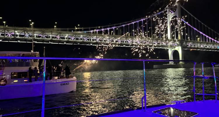 Fuegos artificiales sobre un puente con un barco en primer plano por la noche.