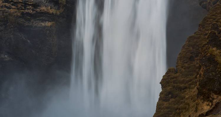 Gros plan d'une cascade puissante entourée de falaises rocheuses.