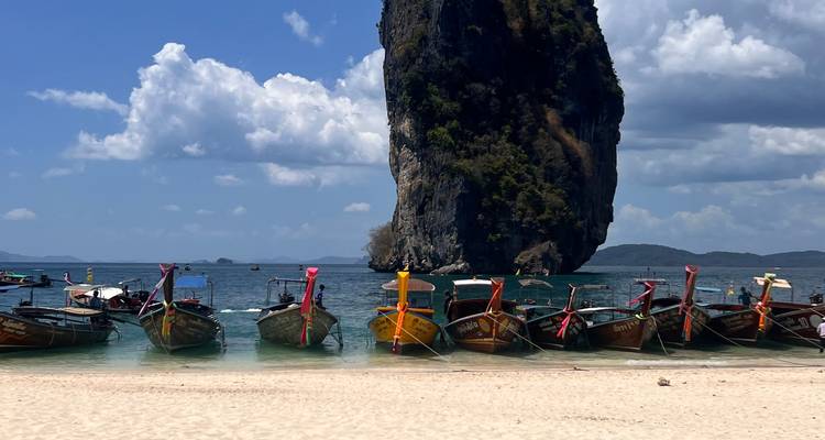 Row of traditional boats near a beach with a towering rock formation.