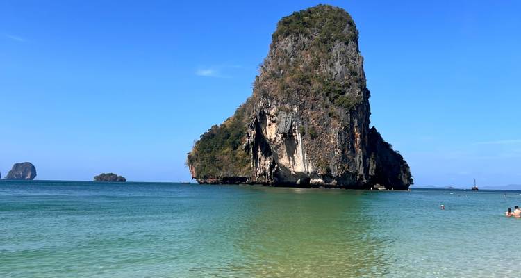 Large rock formation in turquoise waters near a beach.