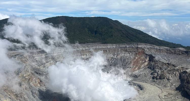 Cratère volcanique fumant avec des montagnes luxuriantes.