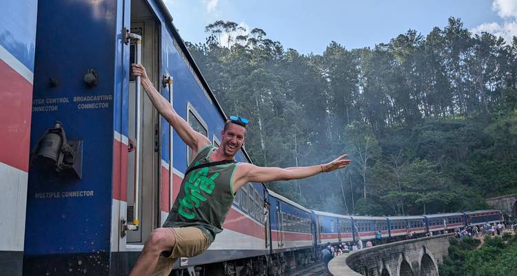 Personne qui se penche de manière ludique à l'extérieur d'un train en marche avec une forêt en arrière-plan.