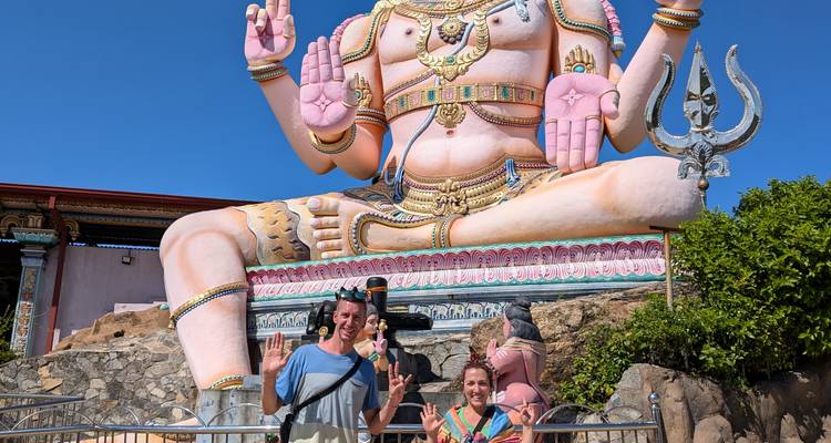 Deux personnes posent devant une grande statue de divinité hindoue rose.
