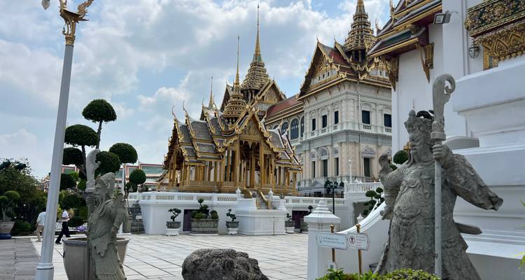 Groot Paleis in Bangkok met standbeelden en bomen.