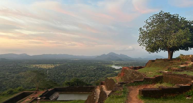Paysage montagneux avec un arbre solitaire et des ruines au coucher du soleil.