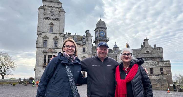 Three people standing in front of a historic castle.