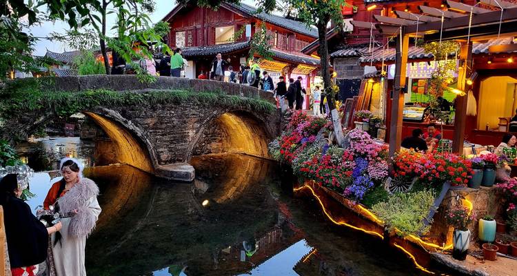 Scenic view of a traditional bridge over a stream with flowers and people.