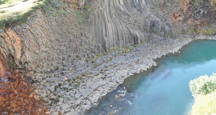 Hexagonal basalt columns by a turquoise pool.
