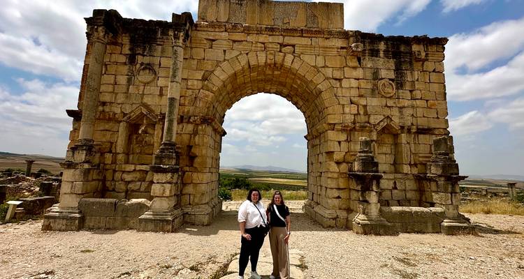 Two people standing under an ancient stone archway.