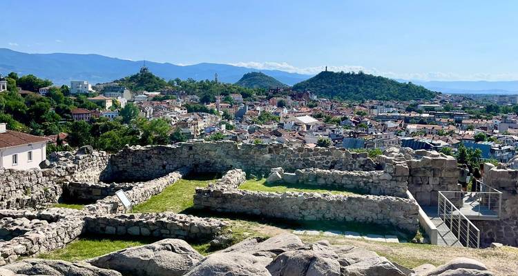 Vue panoramique de ruines antiques avec un paysage urbain et des montagnes en arrière-plan.