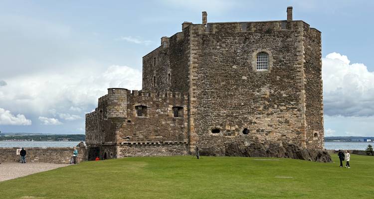 Un château de pierre historique surplombant un plan d'eau, avec des terrains herbeux et des gens qui se promènent à proximité.