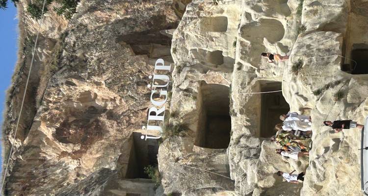People visiting a rock formation with 'Ürgüp' sign.