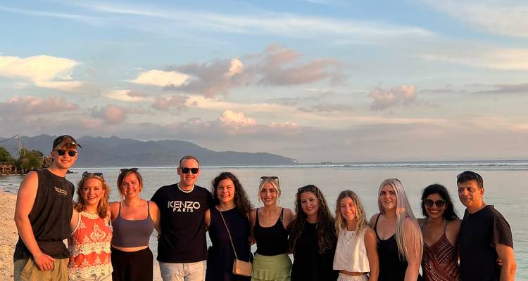 Group of friends smiling in front of a beach and setting sun.