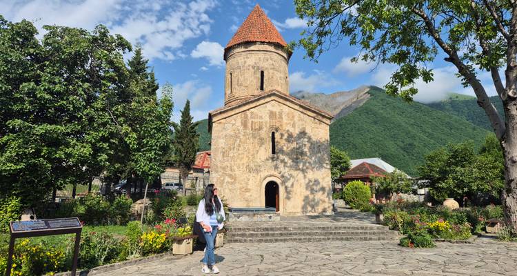 Femme debout devant une église historique avec des montagnes en arrière-plan.