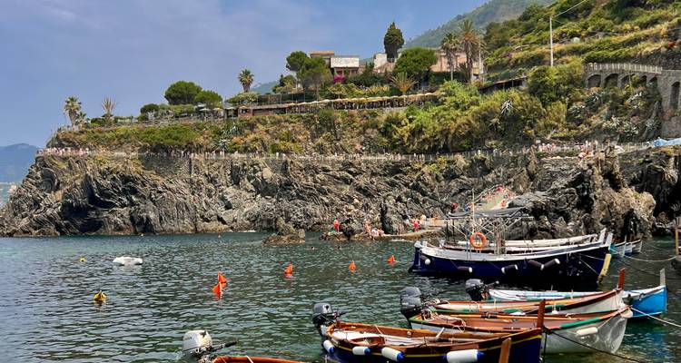 Côte rocheuse avec plusieurs petites embarcations dans l'eau et des personnes sur les rochers.
