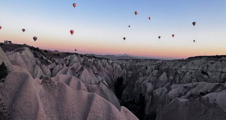 Heteluchtballonnen boven rotsachtig landschap tijdens zonsondergang.