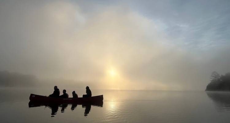 Canoe with people at sunrise on a foggy lake.