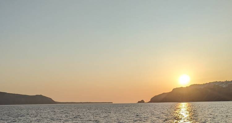 Vue du coucher de soleil sur la mer avec des reliefs au loin.