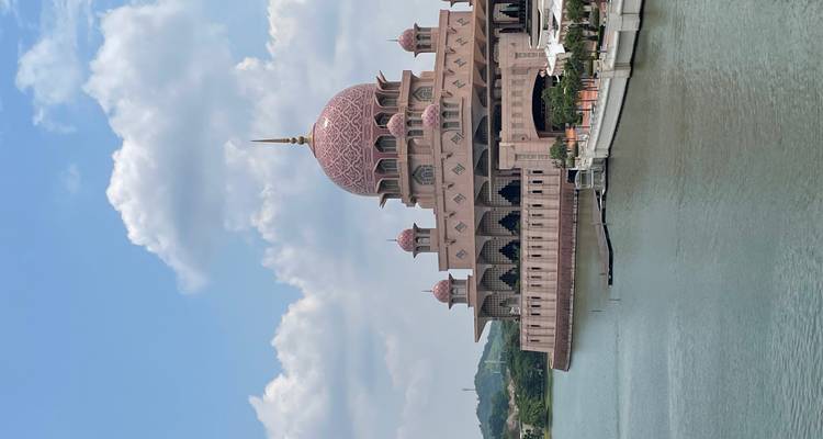 Pink mosque by the water under a blue sky with clouds.
