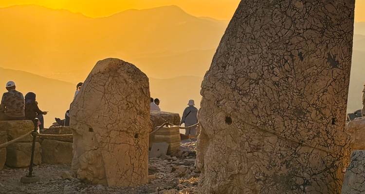 Vue du coucher de soleil sur des statues de pierre et des gens assis sur une colline.
