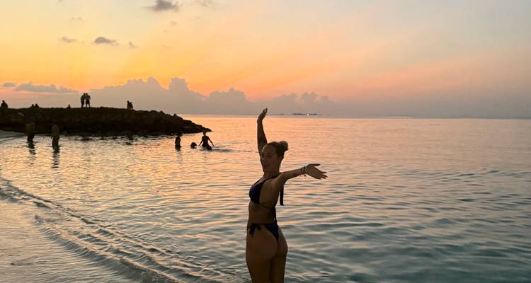 Person standing in the ocean at sunset, posing in swimwear.
