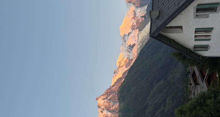 Sunrise over mountain peaks with a house roof in the foreground.