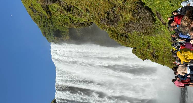 Multitud observando una cascada alta en un entorno verde y exuberante.