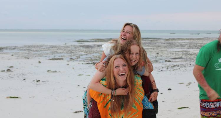 Friends playfully posing on a sandy beach with shallow water.