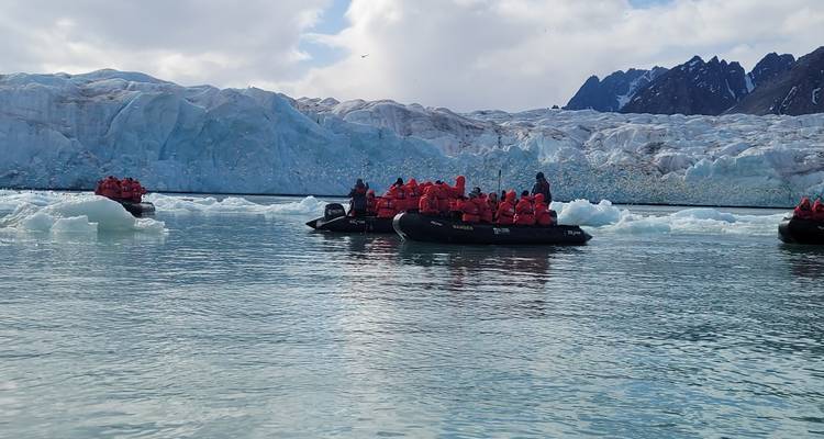 People in boats with life vests exploring a glacier area.
