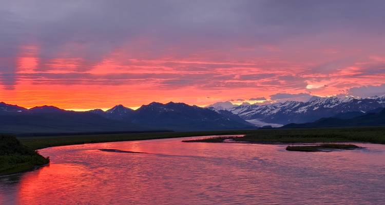 Coucher de soleil vibrant sur la rivière avec des montagnes enneigées.