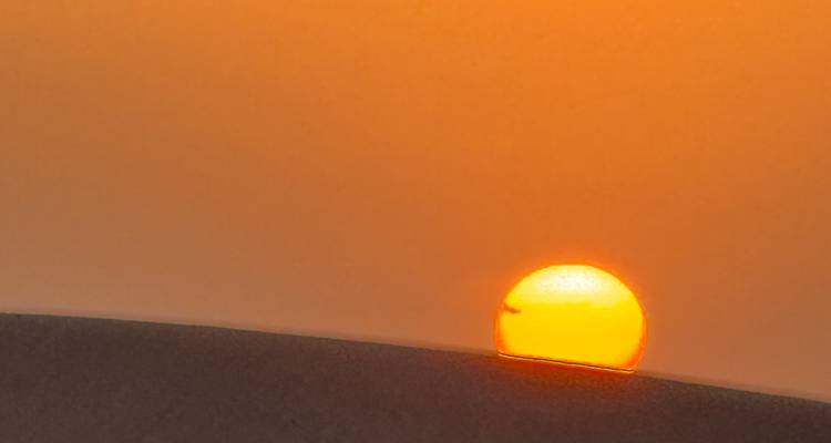 Close-up of the sun setting over a sand dune