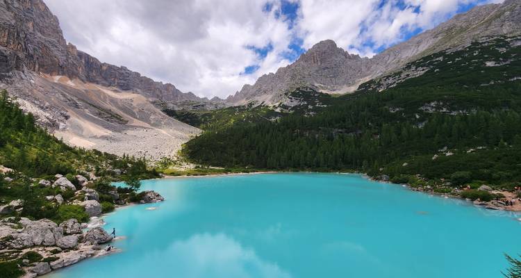 Turquoise lake surrounded by mountains under a partly cloudy sky.