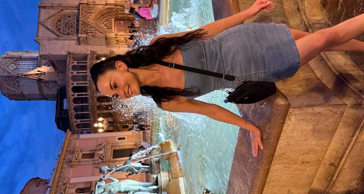 Femme posant près d'une fontaine dans un cadre nocturne animé dans un quartier historique.